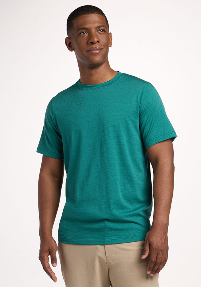 Man in Woolx Endurance Tee - Woodland Mini Stripe and beige pants stands against a white background, looking aside. | Trell is 6’2”, wearing a size M
