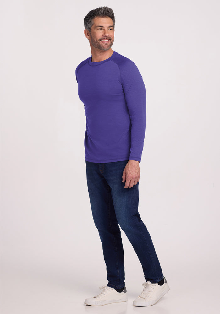 Man smiling in a Woolx Essential Tee - Berry Indigo, dark jeans, and white sneakers against a plain background.
