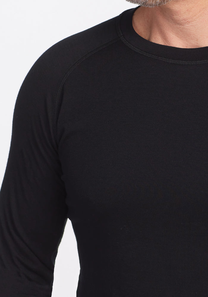 The individual is dressed in the Essential Tee - Black by Woolx, a sleek long-sleeve crafted from luxurious Merino wool. Only the torso and part of the neck stand out crisply against the plain white background.