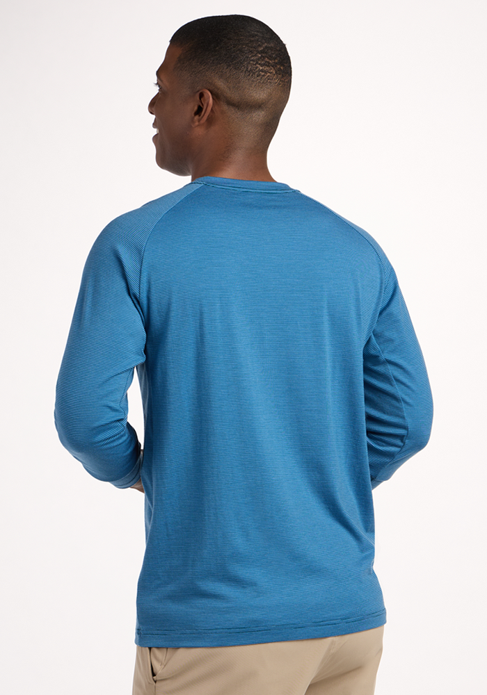 A man, seen from behind in a Woolx Essential Tee - Coastal Mini Stripe and beige pants, stands relaxed against a white background. The temperature-regulating Merino wool fabric ensures comfort wherever you go.