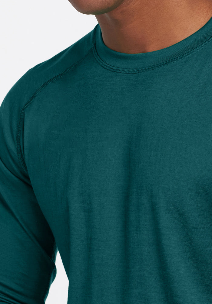 A person wears the Woolx Essential Tee in Riverbank Green; only their neck, shoulder, and torso are visible.