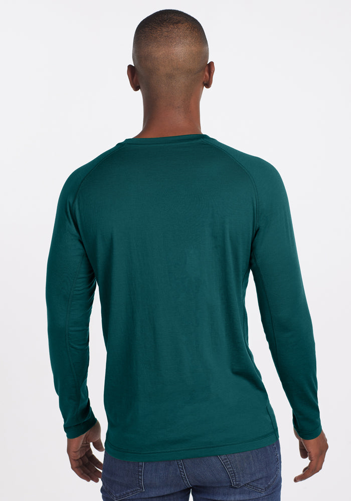 A man in a Woolx Essential Tee • Final Sale - Riverbank Green and jeans faces away from the camera on a white background.