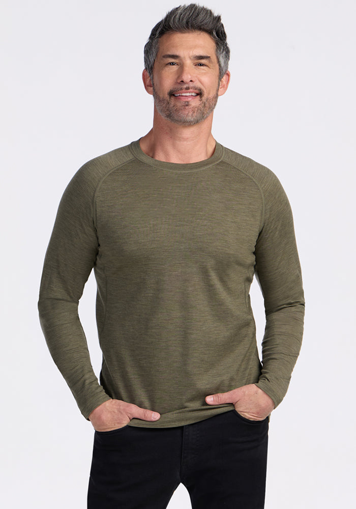 Man smiling, wearing the Woolx Essential Tee in Sage Olive Melange and black pants, hands in pockets.
