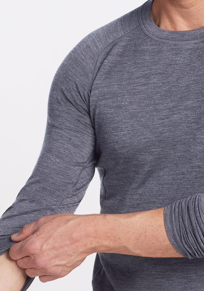 Someone wearing the Woolx Essential Tee in Graphite Heather is rolling up their sleeve, with only their torso and arms visible against a plain white background.