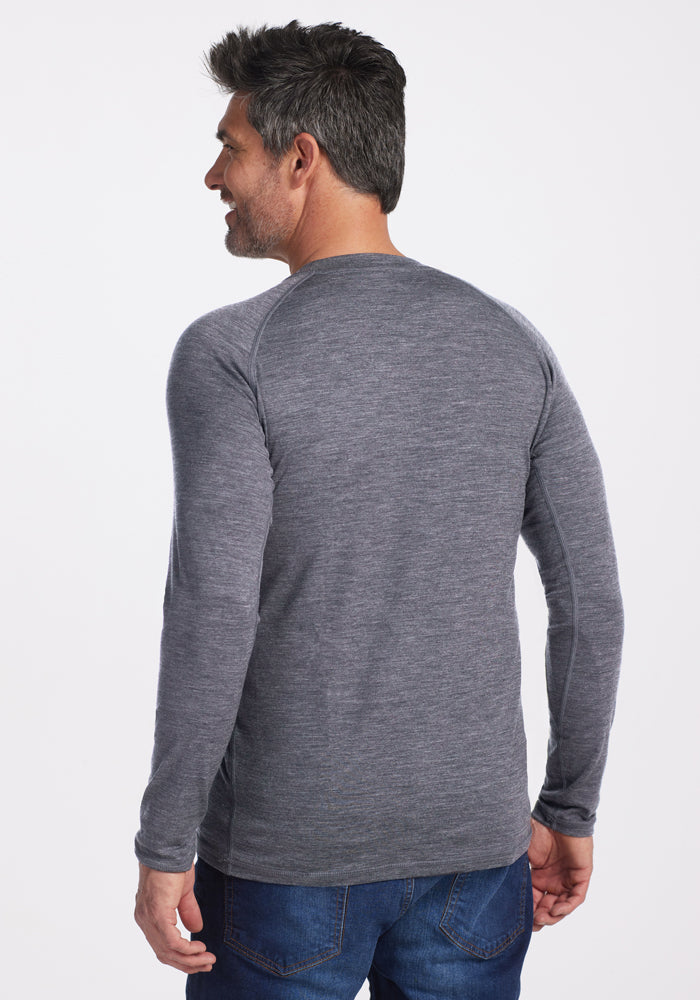 A man with short dark hair faces away, slightly turned left, wearing the Woolx Essential Tee - Graphite Heather. This lightweight athletic tee, crafted from temperature-regulating Merino wool, offers ultimate comfort and style against a plain white backdrop with blue jeans.