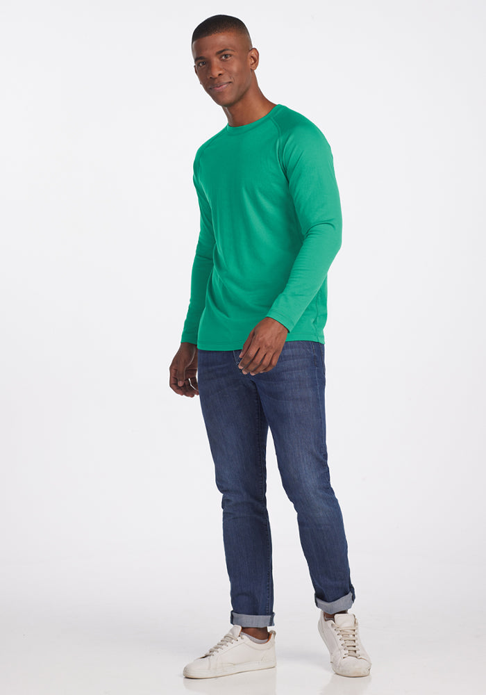 Man wearing Woolx Essential Tee - Jungle, blue jeans, and white sneakers against a plain background.