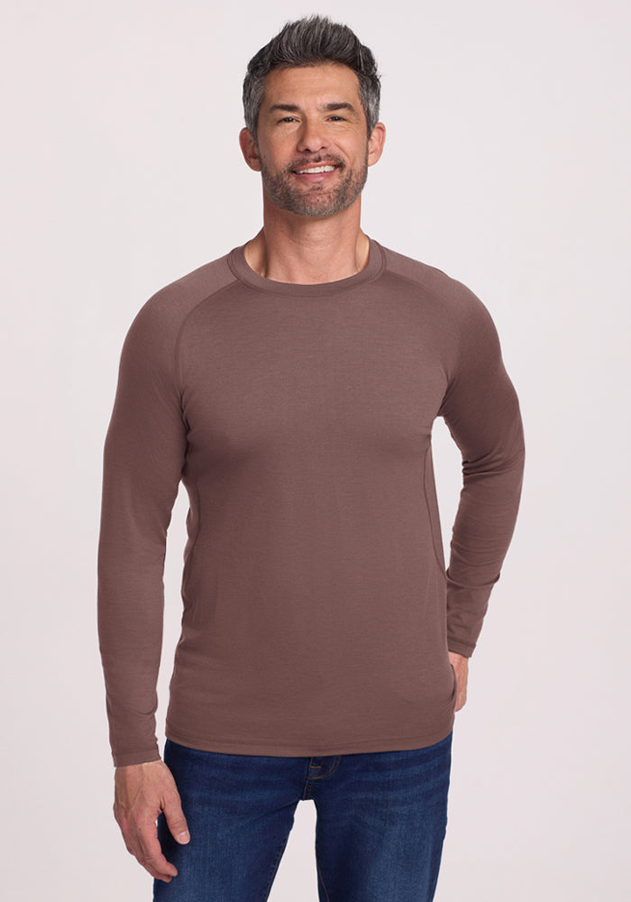 Man wearing a Woolx Essential Tee in Peppercorn and blue jeans, standing and smiling against a plain light background. | Matthew is 6’, wearing a size L