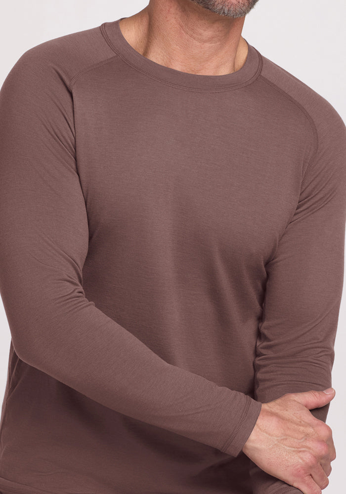 Man wearing a Woolx Essential Tee - Peppercorn, with one arm bent and hand grasping the opposite forearm.