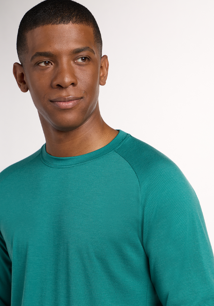 A man wearing the Woolx Essential Tee - Woodland Mini Stripe gazes slightly left with a neutral expression, standing against a plain, light background.
