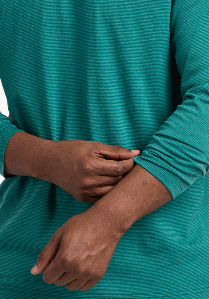 A person is shown from the torso down, adjusting their left sleeve while wearing the Woolx Essential Tee - Woodland Mini Stripe. The background is white.