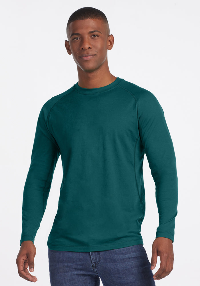 Man wearing a Woolx Essential Tee in Riverbank Green, standing against a plain white background and smiling slightly.