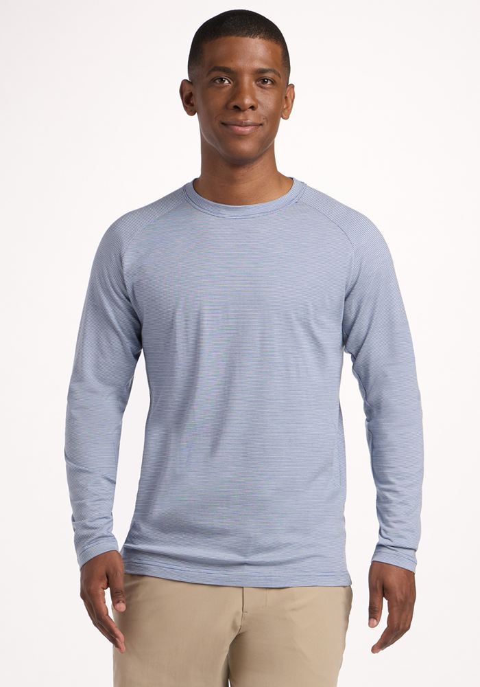 A man wearing the Woolx Essential Tee in Blue Sand Mini Stripe and beige pants stands smiling in front of a plain white background. | Trell is 6’2”, wearing a size M