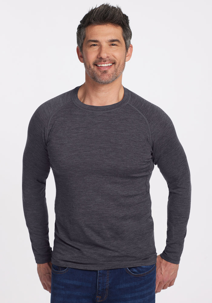 A smiling man in Woolx’s Essential Tee • Final Sale - Cinder Melange stands before a white background in blue jeans.