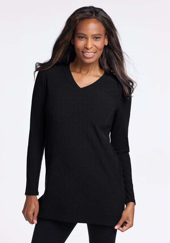 A person with long hair smiles while wearing the Evie Tunic - Black from Woolx. The temperature-regulating Merino wool fabric ensures comfort, accentuated by the plain white background.
