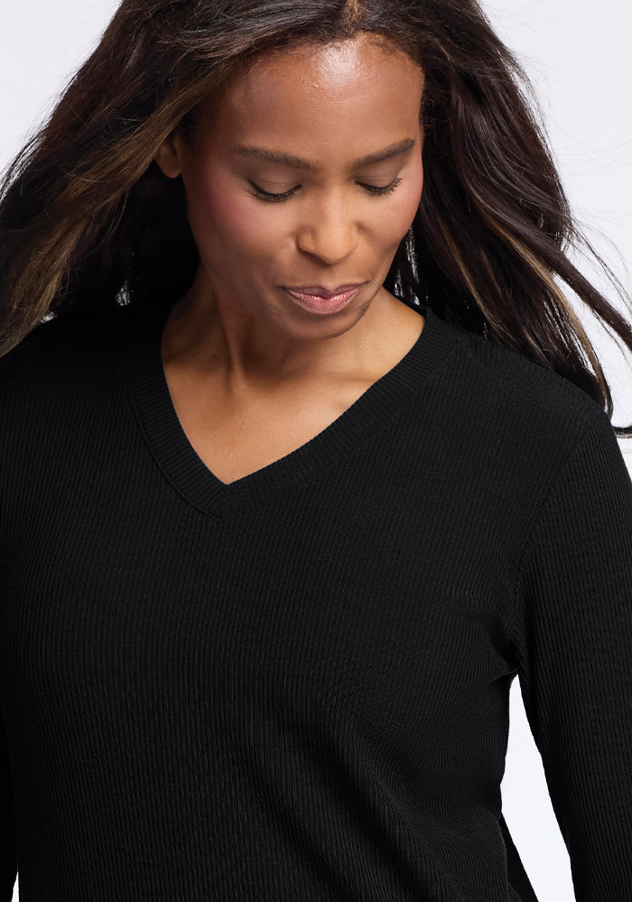 A woman with long hair is wearing the Evie Tunic in black, a cozy, temperature-regulating V-neck sweater from Woolx. Made from Merino wool, she gazes down with a serene expression against a neutral background.