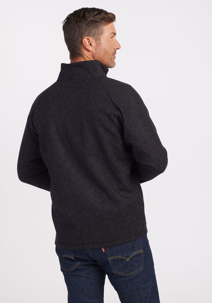 A man is facing away from the camera, clad in a dark gray Fairbanks Jacket by Woolx, expertly crafted from Merino Wool, paired with blue jeans. The jacket's minimalistic design pops against the plain white background.