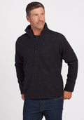 A man with short hair is wearing a Woolx Fairbanks Jacket in Carbon Black, featuring a zip-up design with a minimalistic aesthetic. Paired with jeans, he stands against a plain background, looking to the side with one hand in his pocket, highlighting the refined simplicity of his attire. | Lee is 6’, wearing a size M