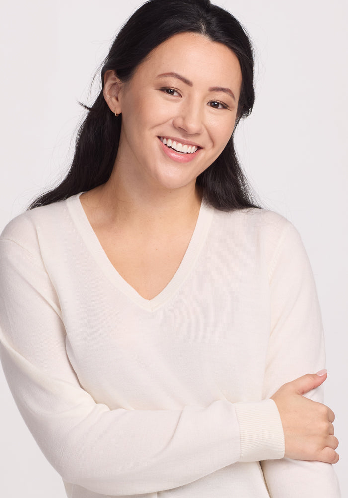 A person with long dark hair smiles warmly, wearing the breathable Dewdrop Pearl Francesca Sweater by Woolx. The background is plain white.