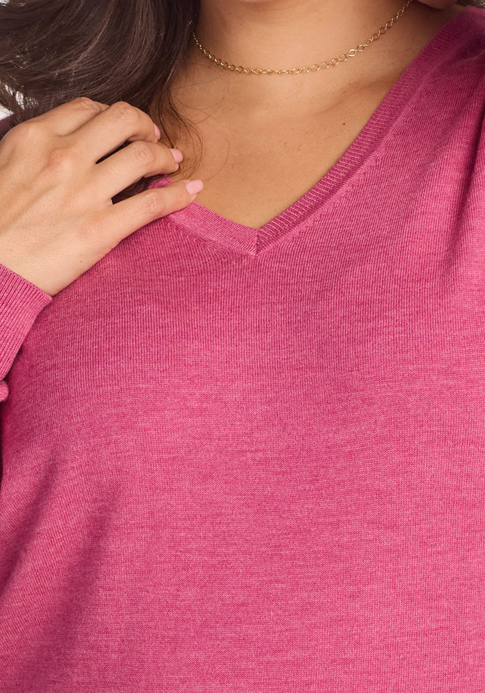 A person in the Woolx Francesca Sweater in Wild Salmon, wearing a gold chain necklace, holds their hand by their collarbone; only their lower face, neck, and upper chest are visible.