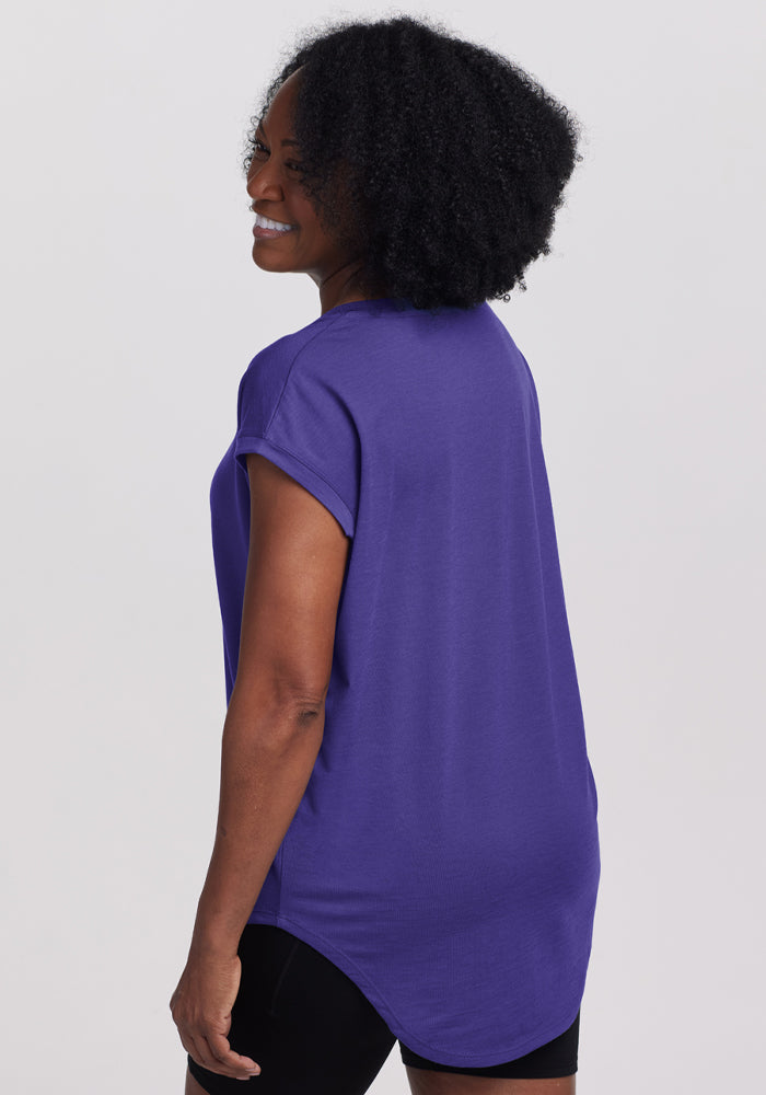 Woman with curly hair smiles over her shoulder in the Woolx Gabi Tunic Top - Berry Indigo.