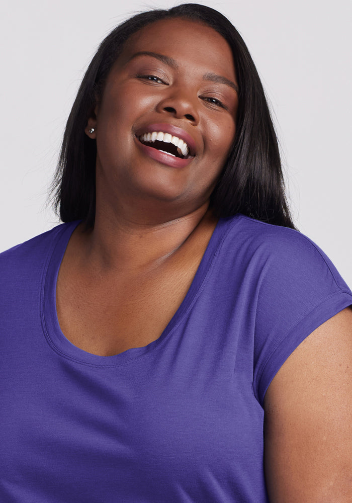 A woman with long dark hair smiles in the Woolx Gabi Tunic Top in Berry Indigo against a light background.
