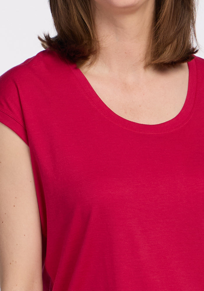 A woman wears the Woolx Gabi Tunic Top in Poppy Spark, a bright pink scoop-neck, short-sleeve style.