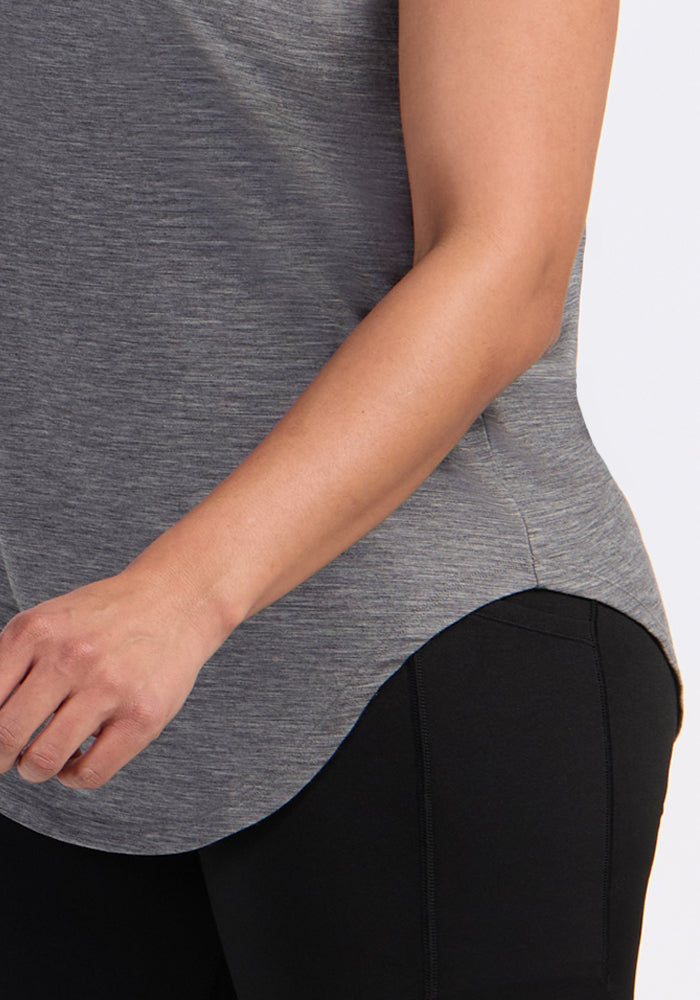 A person is shown from shoulders to mid-thigh wearing the Woolx Gabi Tunic Top in Graphite Heather with black pants; their left arm is slightly bent and the hand is partially visible.