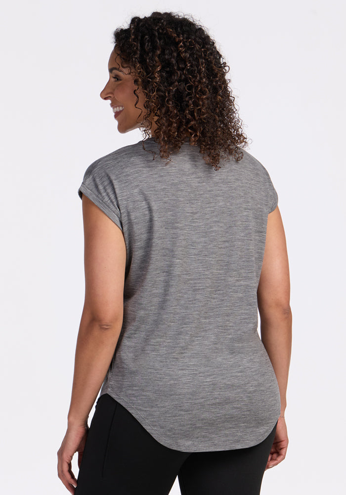 A woman with curly hair is shown from the back, smiling in the Woolx Gabi Tunic Top - Graphite Heather and black pants, standing against a plain white background.