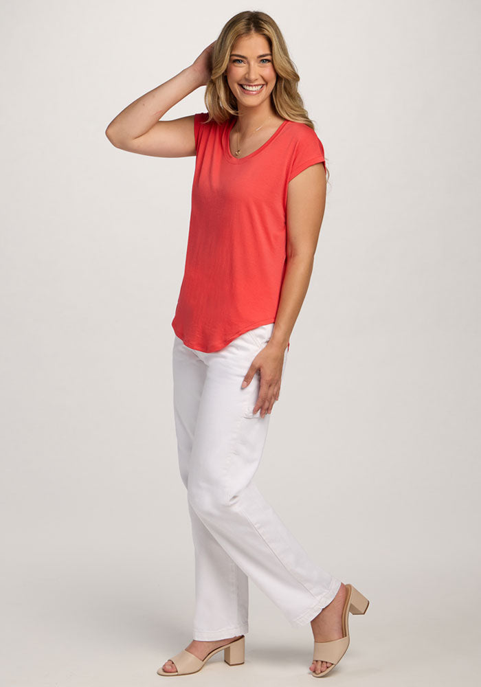 Woman in Woolx Gabi Tunic Top - Hibiscus, white pants, and beige heels poses with one hand in her hair.
