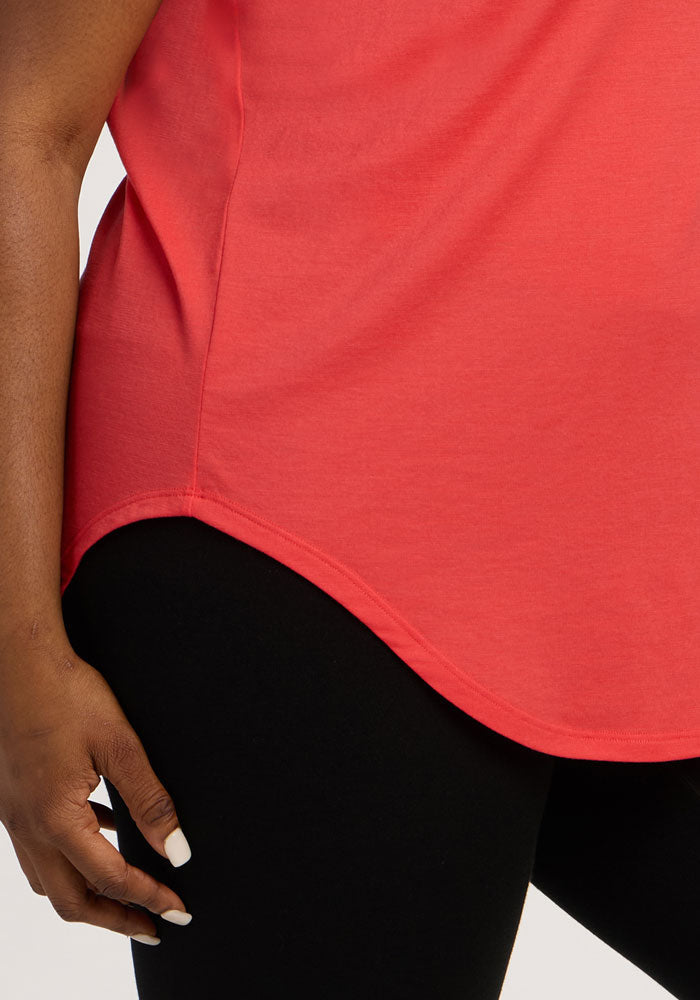 A person wears the Woolx Gabi Tunic Top - Hibiscus and black pants, shown waist down with a hand by their side.