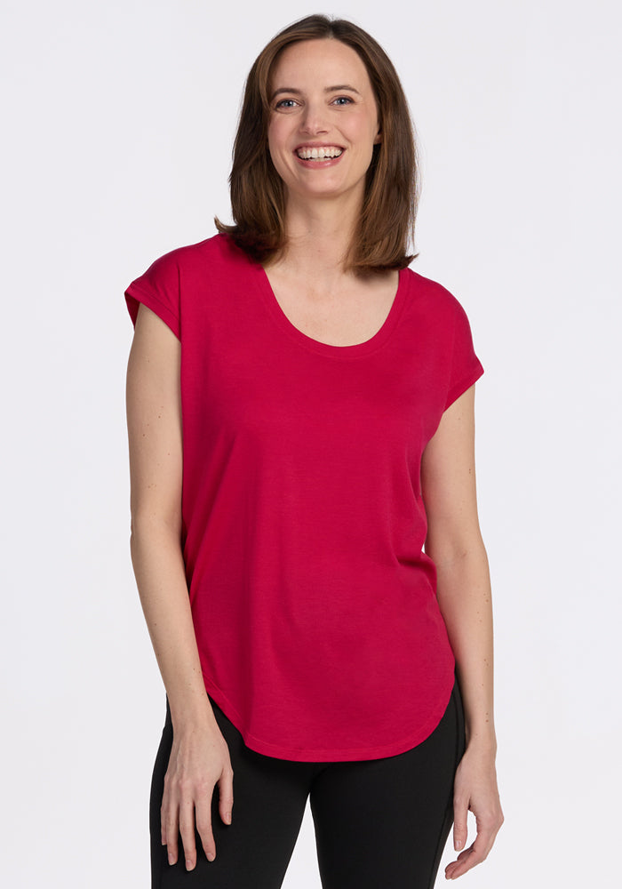 A woman with shoulder-length brown hair smiles, wearing the Woolx Gabi Tunic Top in Poppy Spark and black pants.