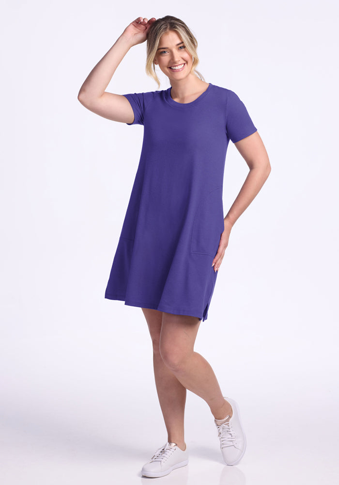Woman smiles in the Woolx Georgie Dress - Berry Indigo, a wrinkle-resistant knee-length travel dress, paired with white sneakers.