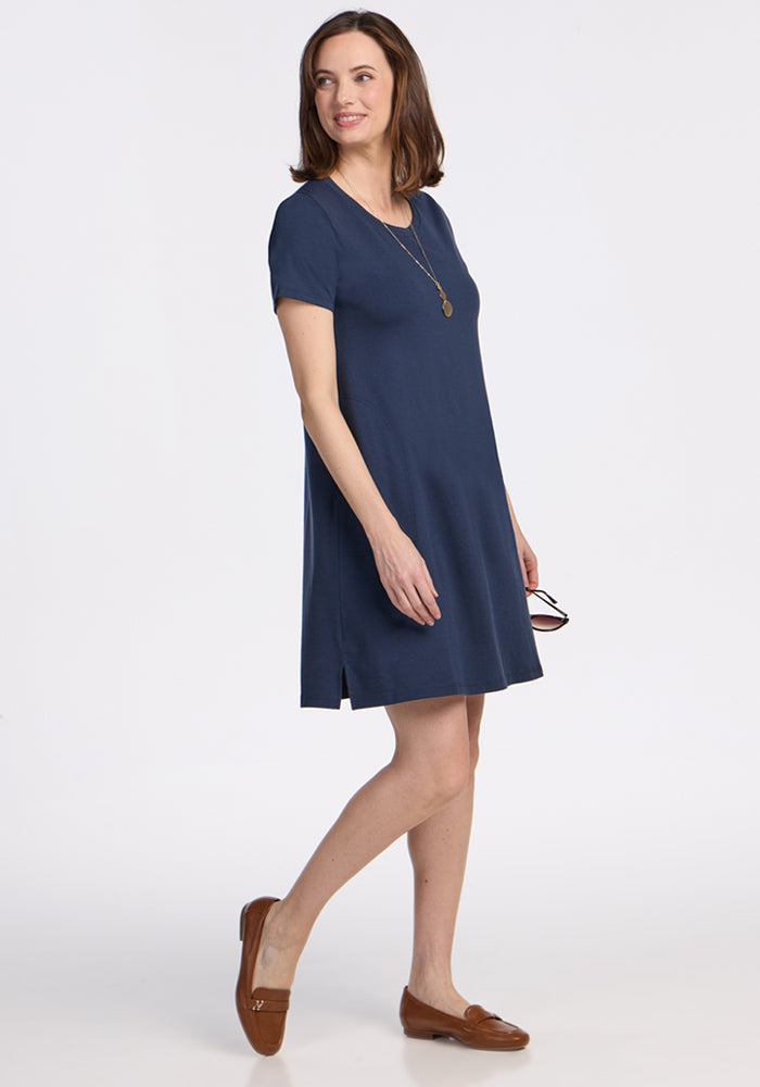 Smiling woman in Woolx Georgie Dress • Final Sale - Deep Navy, brown loafers, necklace, holding glasses, walking.