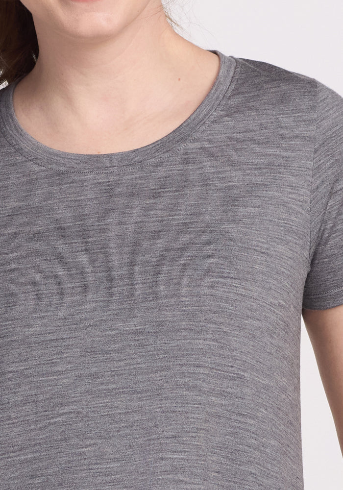 A person is partially visible against a neutral background, wearing the Woolx Georgie Dress in Graphite Heather. The image shows only their upper torso and part of their face without distinct features.