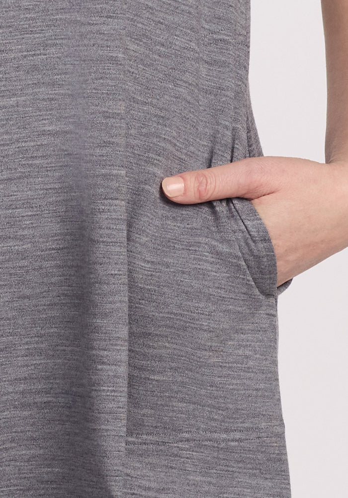 A close-up shows a person wearing the Woolx Georgie Dress in Graphite Heather, with a right hand placed in the side pocket. The merino wool's textured, moisture-wicking fabric adds comfort as their arm rests relaxedly.