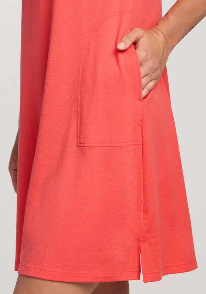 A person wears the Woolx Georgie Dress - Hibiscus, with a hand in the pocket, featuring a side slit and seam details.