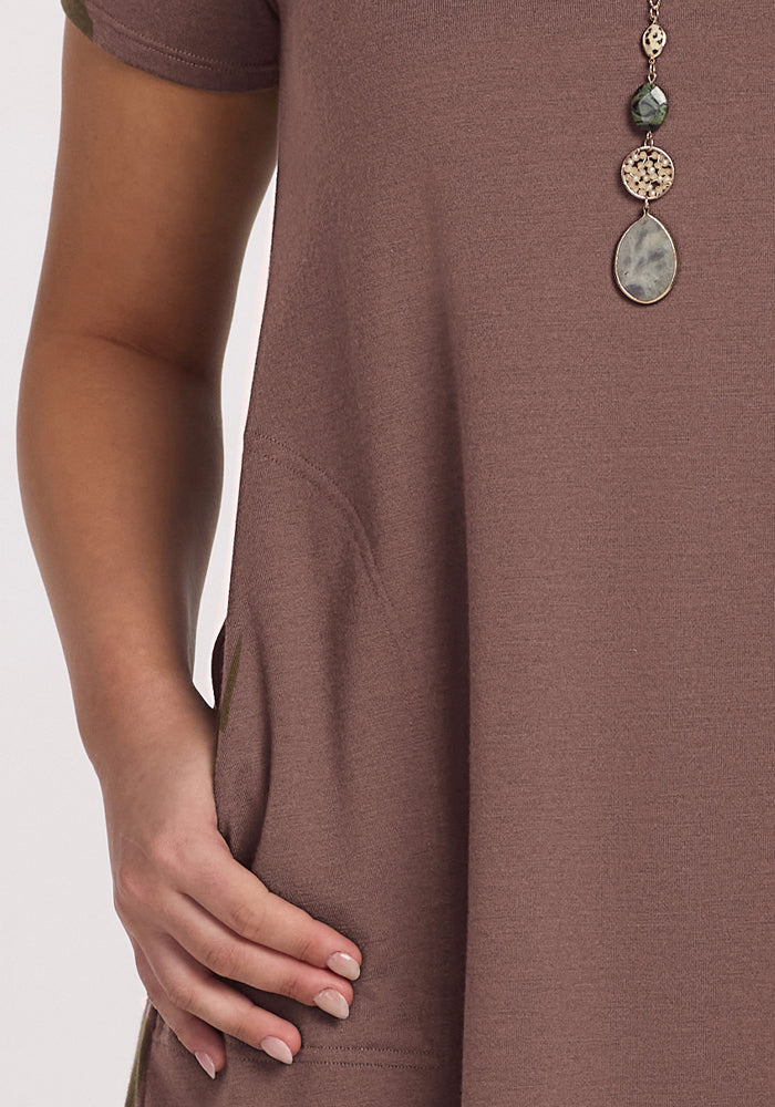 A person in the Woolx Georgie Dress - Peppercorn with one hand in a pocket and a long beaded necklace.