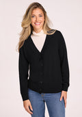 A woman with long blonde hair smiles against a light background, wearing a Woolx Gia Sweater in black over a white turtleneck and blue jeans, enjoying the cozy, odor-resistant comfort of this classic Merino wool style. | Ariana is 5'11", wearing a size S