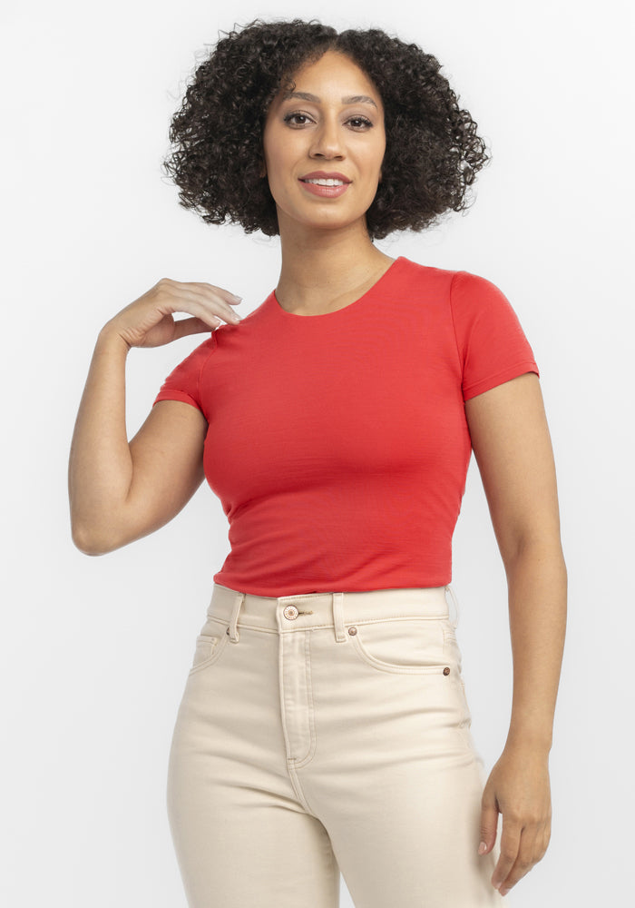 Woman with curly hair in the Woolx Gracie Bodysuit - Hibiscus and high-waisted beige pants, smiling at the camera. | Tori is 5'7", wearing a size S
