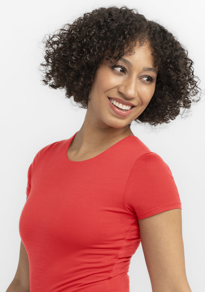 Smiling woman in the Woolx Gracie Bodysuit - Hibiscus, looking left against a white background.
