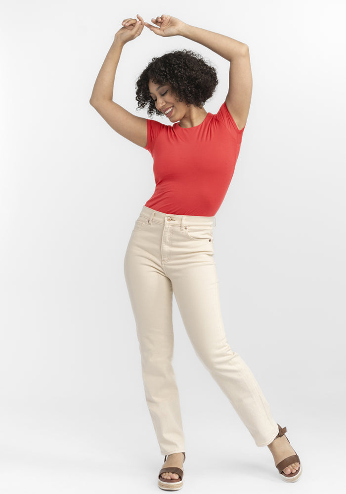 Smiling woman in the Woolx Gracie Bodysuit - Hibiscus and beige pants poses with arms raised against a white background.