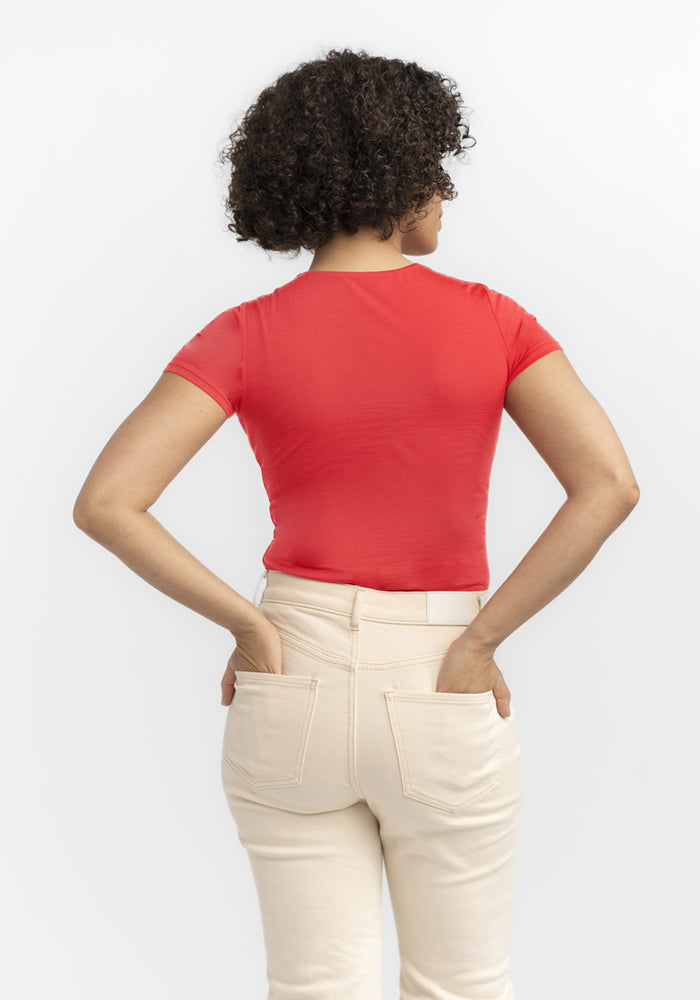 A person with curly hair wears the Woolx Gracie Bodysuit - Hibiscus and beige pants, hands in pockets, facing away.