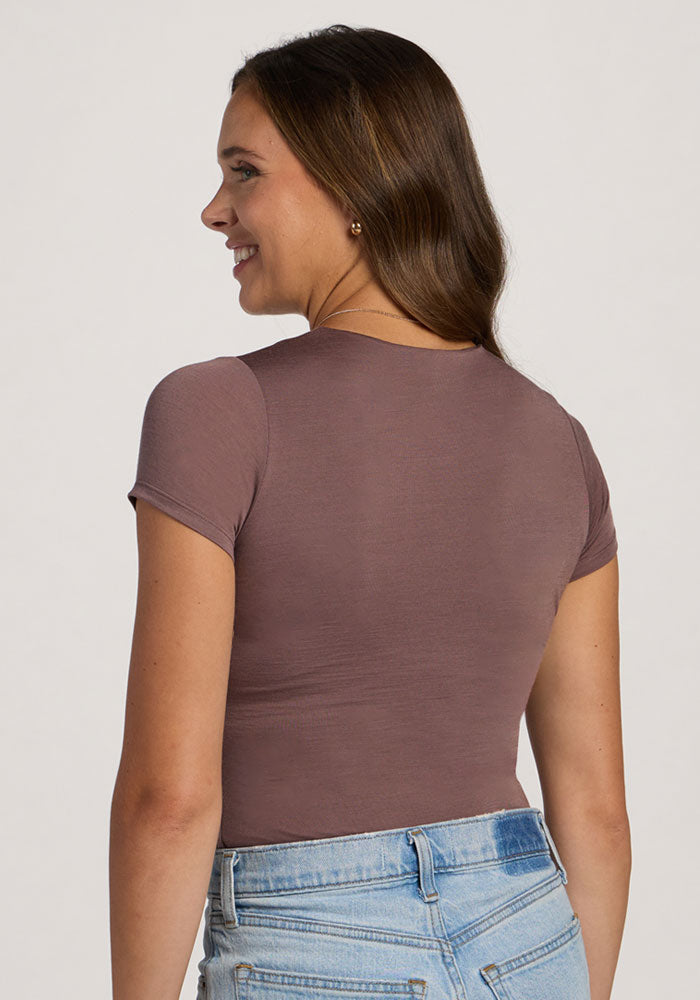 Woman with her back turned, smiling slightly in a Woolx Gracie Bodysuit - Peppercorn and light blue jeans.