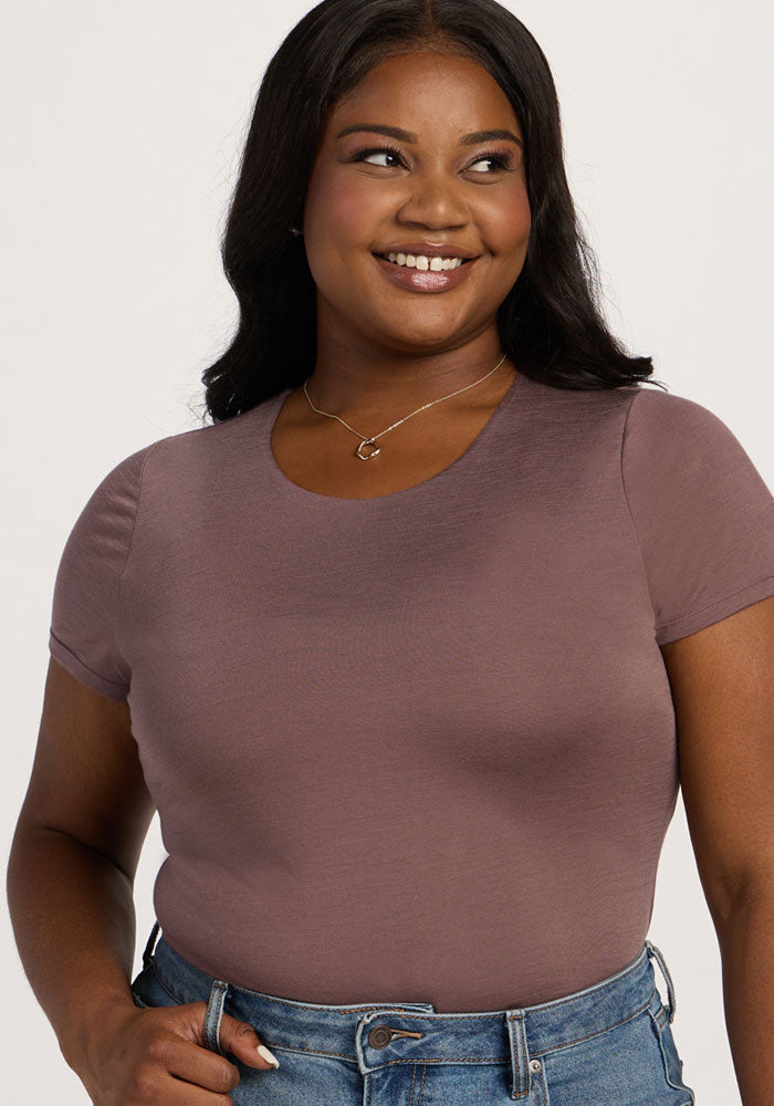 Smiling woman in the Woolx Gracie Bodysuit - Peppercorn and jeans, standing against a plain background.