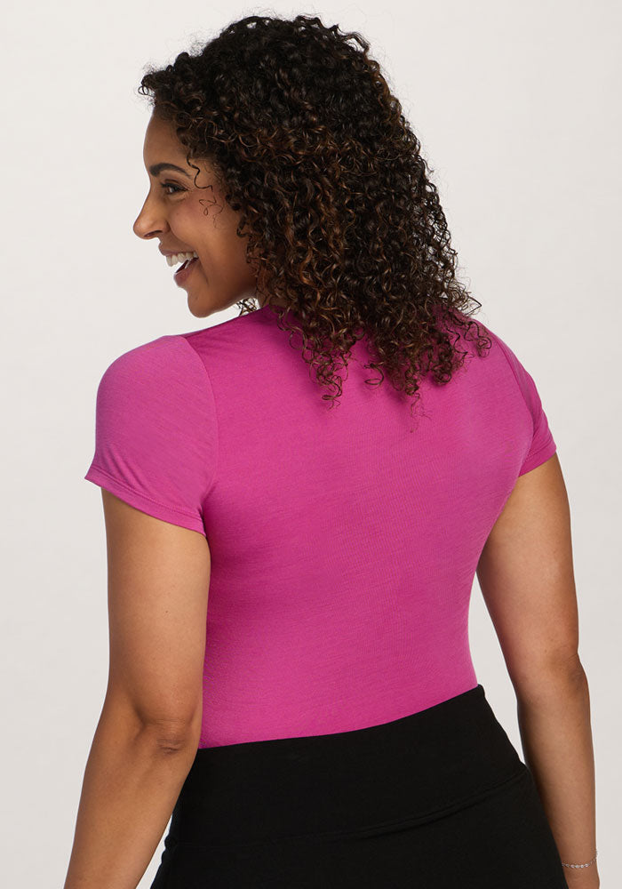 Woman with curly hair smiles, shown from the back wearing Woolx Gracie Bodysuit - Summer Sorbet and black bottoms.