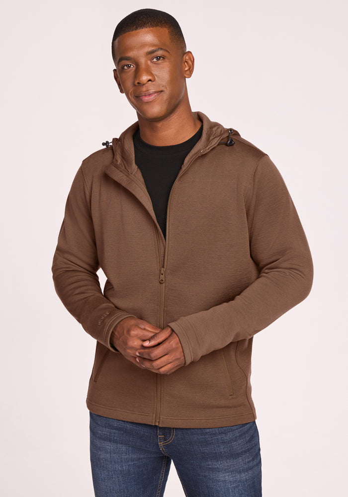 A man in a Woolx Grizzly Sweatshirt • Final Sale - Bourbon Oak stands facing the camera, slight smile, hands loosely clasped. He wears it over a black shirt and blue jeans. A plain light background highlights the sweatshirt’s comfort.