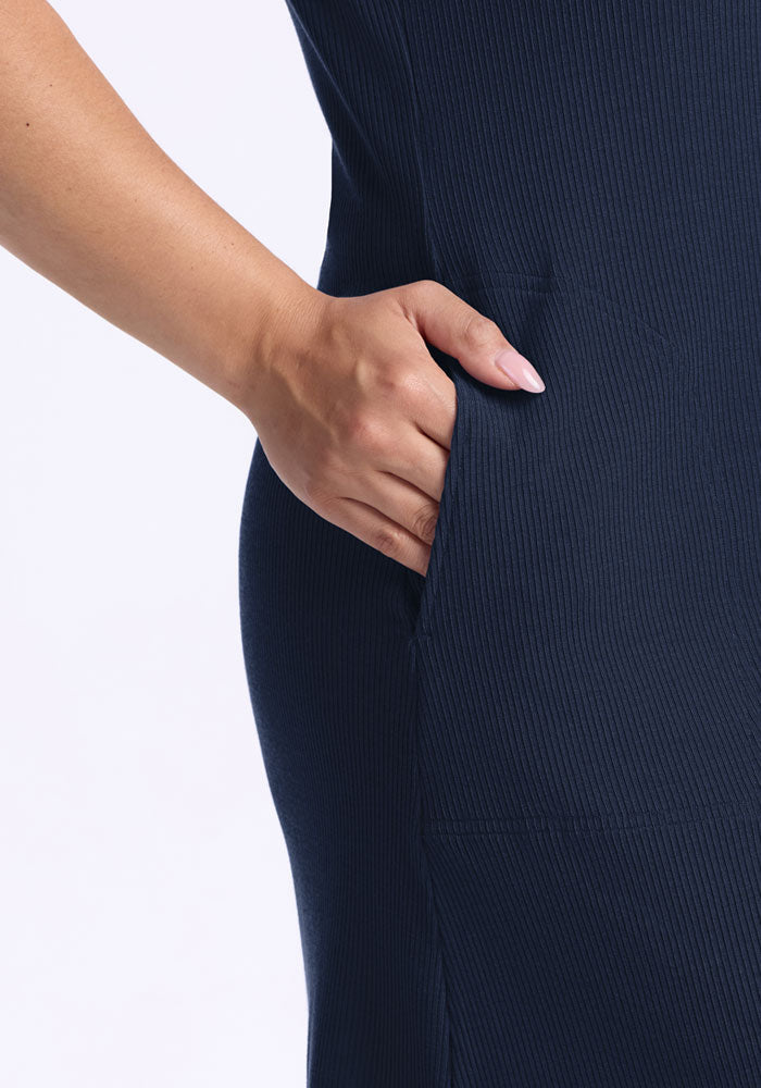 A person slips their hand into the pocket of the Woolx Harlowe Ribbed Dress in Deep Navy.