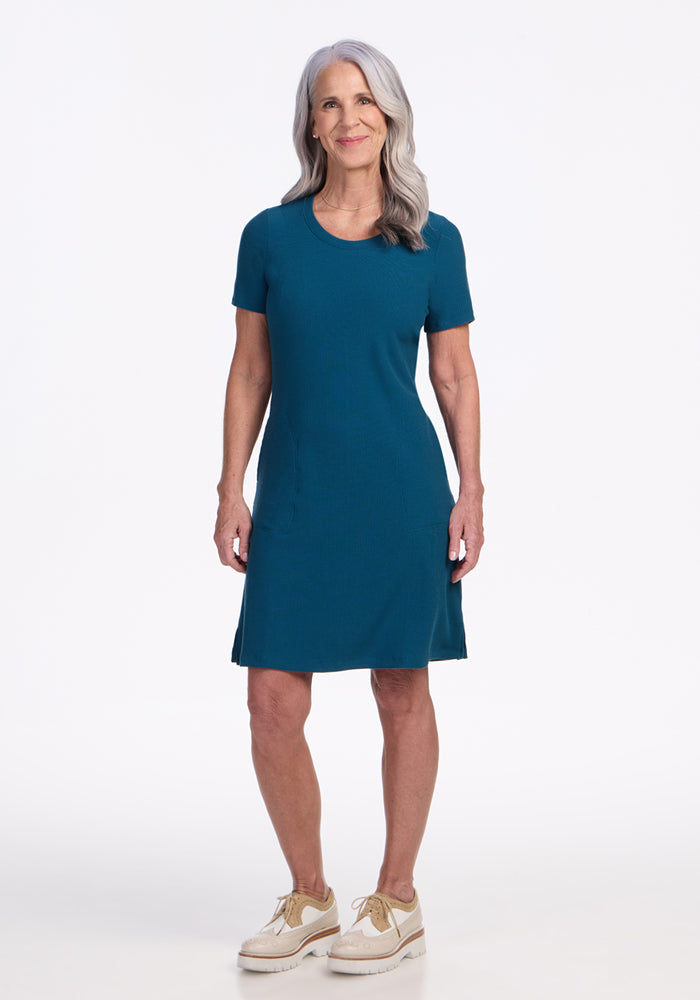 Smiling woman in Woolx Harlowe Ribbed Dress in Moroccan Blue, standing against a white background.