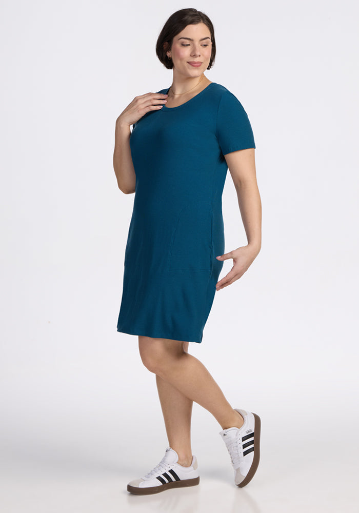 Woman wearing the Harlowe Ribbed Dress in Moroccan Blue by Woolx, standing and smiling on a white background.