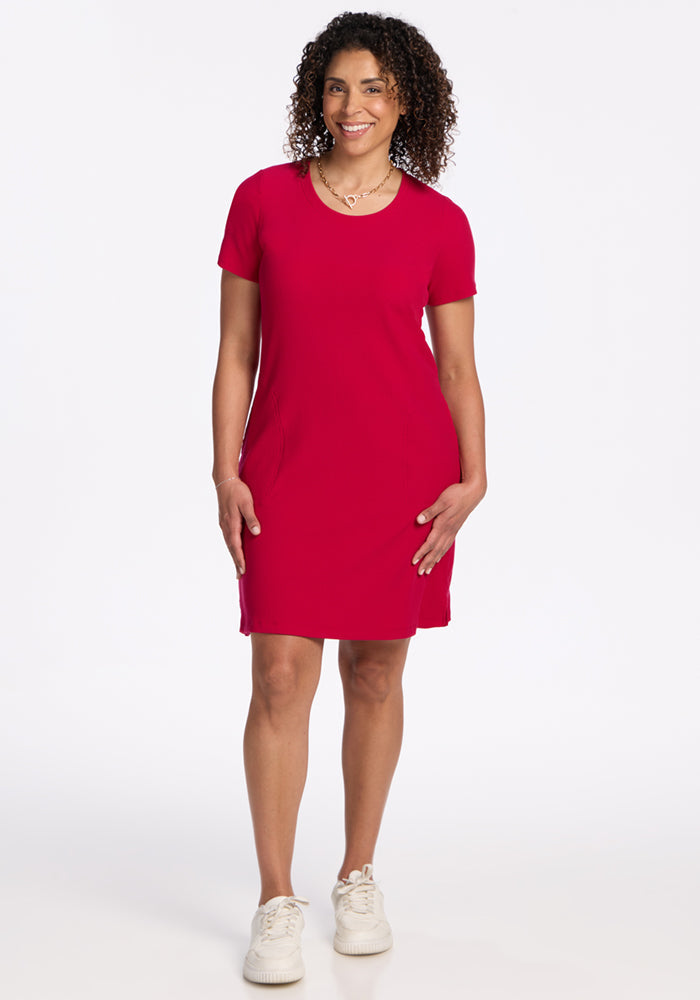 Woman in a Woolx Harlowe Ribbed Dress in Poppy Spark and white sneakers smiles against a white background.